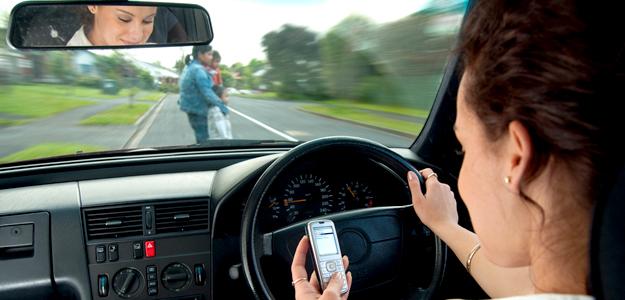 Texting while driving, family crossing road visible in windscreen